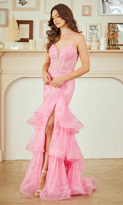 A woman in the Amelia Couture 8062 Long Lace Ruffled Prom Dress stands indoors before a decorated mantelpiece, showcasing its sleeveless design, light pink hue, ruffled details, and front slit.