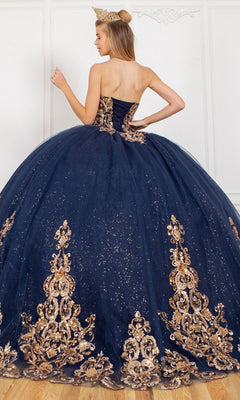 A woman stands with her back to the camera wearing the Quinceanera Ball Gown 8063J, a strapless sweetheart navy blue gown with gold embellishments, glitter tulle skirt, and a gold crown.