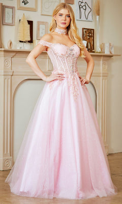 A woman in the Amelia Couture 8064 long prom dress, light pink and off-the-shoulder with a fitted embellished bodice, stands indoors before a cream-colored fireplace.