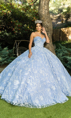 A woman in the Cinderella Couture 8071J quinceanera dress—a light blue, strapless ball gown with white embroidery and beaded fringe—wears a tiara and stands outdoors beside a tree.