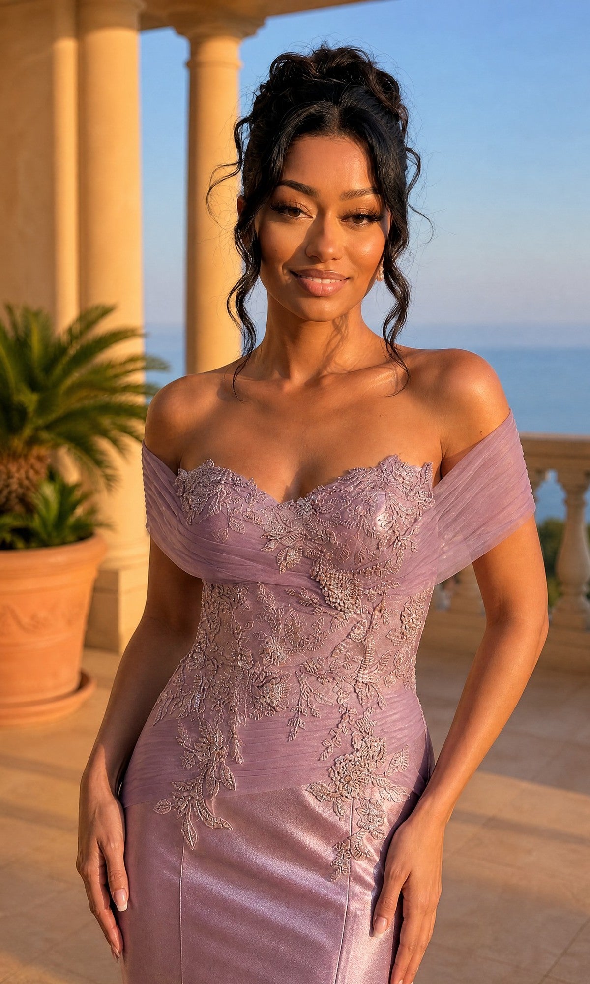 A woman in the Amelia Couture 8074 long prom dress poses on a sunny terrace with columns, a potted plant, and an ocean view in the background.