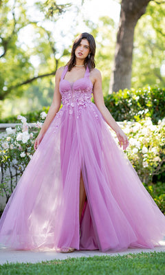 A woman stands outdoors in the floor-length Cinderella Couture 8076J, a lavender halter prom dress featuring floral embellishments and a tulle skirt. Greenery and white flowers decorate the background.