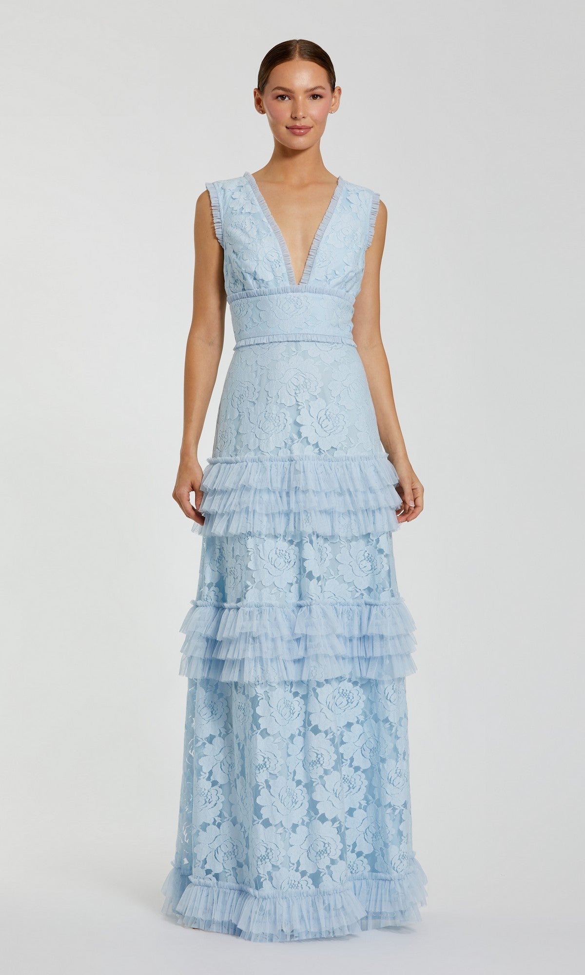 A woman stands against a plain light background wearing the Mac Duggal 8078 Long Formal Dress in powder blue—a sleeveless, floor-length gown crafted from delicate floral lace, featuring a deep V-neck and a tiered ruffle skirt.