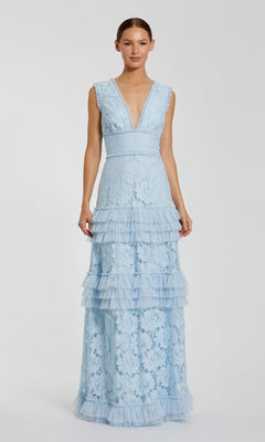 A woman stands against a plain light background wearing the Mac Duggal 8078 Long Formal Dress in powder blue—a sleeveless, floor-length gown crafted from delicate floral lace, featuring a deep V-neck and a tiered ruffle skirt.
