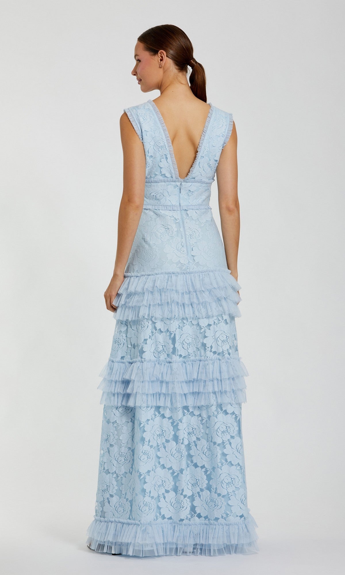 A woman, shown from behind, wears the Mac Duggal 8078 Long Formal Dress—a light blue sleeveless gown featuring floral lace and tiered ruffles—standing against a plain white background.