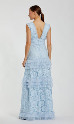 A woman, shown from behind, wears the Mac Duggal 8078 Long Formal Dress—a light blue sleeveless gown featuring floral lace and tiered ruffles—standing against a plain white background.