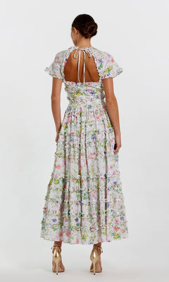 A woman stands facing away, wearing the Mac Duggal 8079 Midi Wedding Guest Dress with short sleeves, an open back, and a fit-and-flare silhouette, elegantly paired with gold high-heeled shoes.
