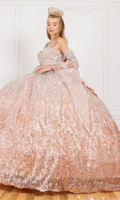 A woman in the Quinceanera Ball Gown 8080J, adorned with large crystal beads, silver sequins, and a crown, stands before a white wall.