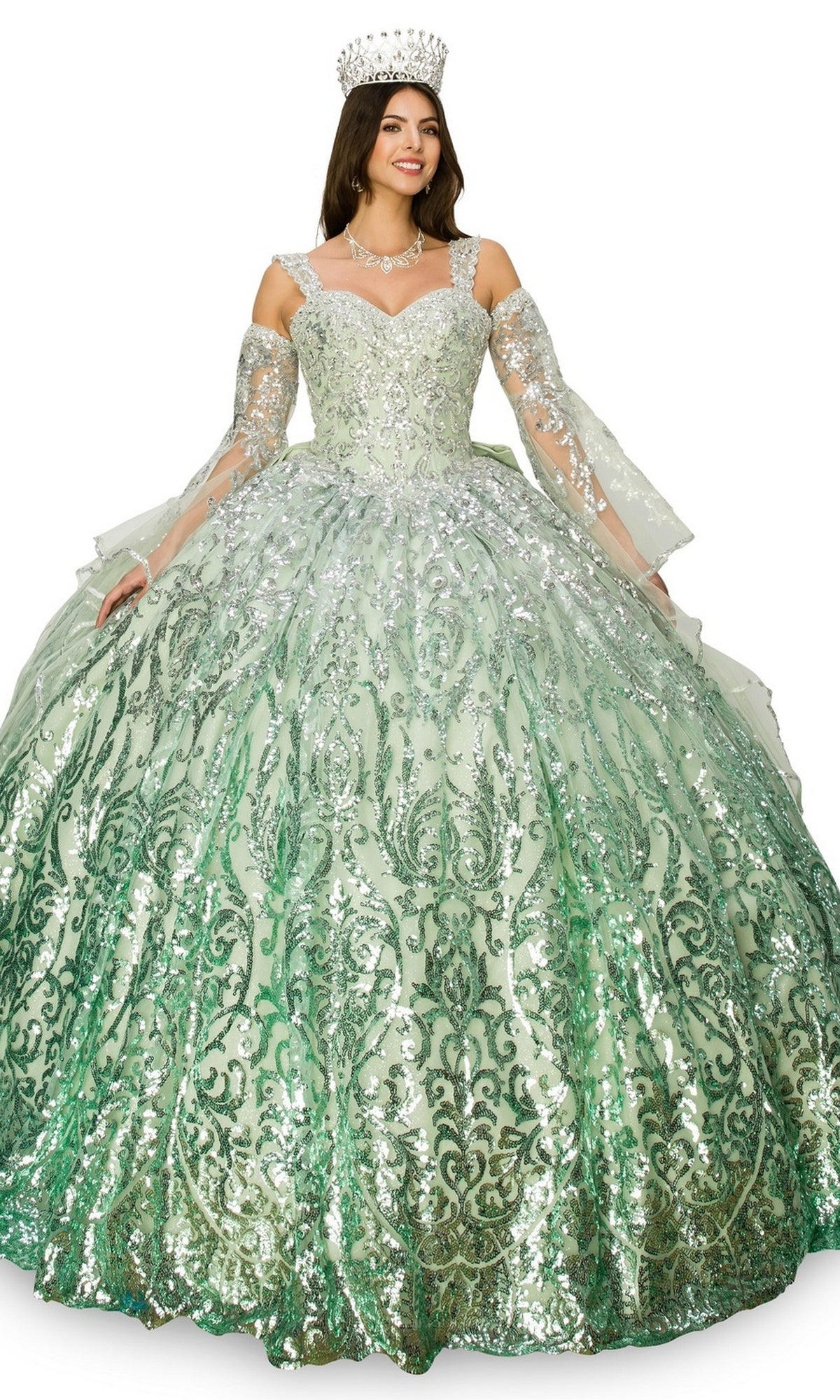 A woman smiles while wearing the Quinceanera Ball Gown 8080J, a sparkling light green dress with silver patterns, matching gloves, necklace, and jeweled crown.
