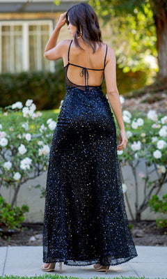 A woman stands outdoors, surrounded by white flowers and greenery, wearing the Backless Sequin Prom Dress: Cinderella Couture 8081J with thin straps and an open back.