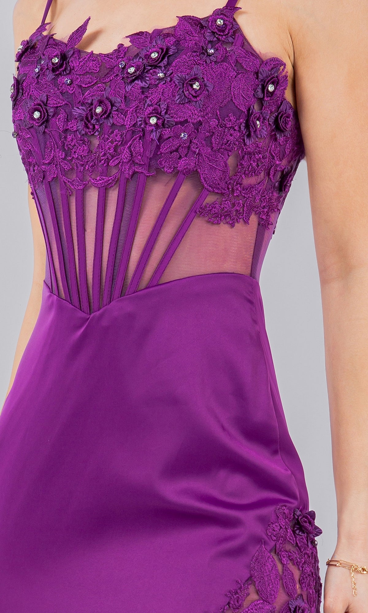 A close-up of the Long Corset Prom Dress: Cinderella Couture 8085J in purple, featuring floral lace, beaded embroidery, and sheer mesh panels, shown worn with a bracelet.