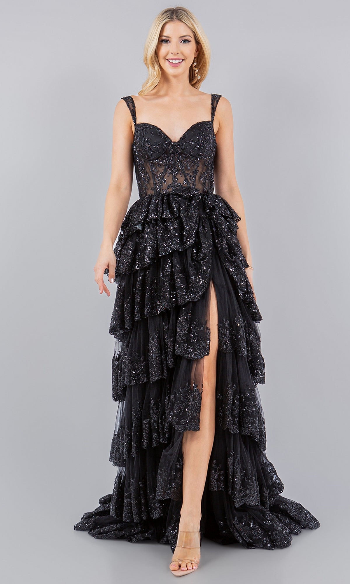 A woman models the Cinderella Couture 8093J, a sleeveless black ruffled tiered prom dress with sequin accents and a high front slit, set against a plain grey background.
