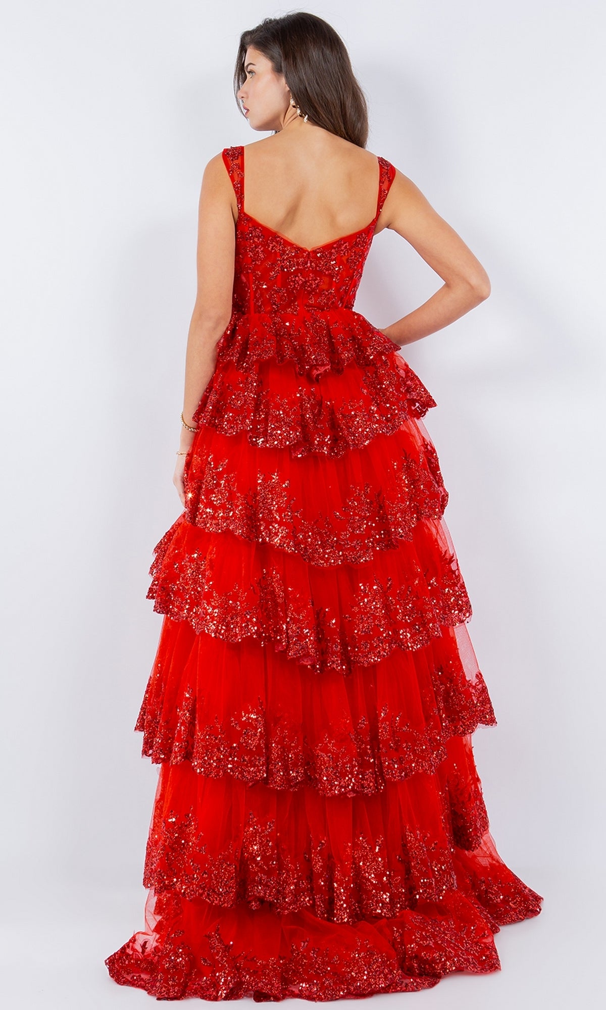 A woman faces away, wearing the Cinderella Couture 8093J Ruffled Tiered Prom Dress in red with shimmering sequins and multiple ruffle tiers, set against a plain light background.