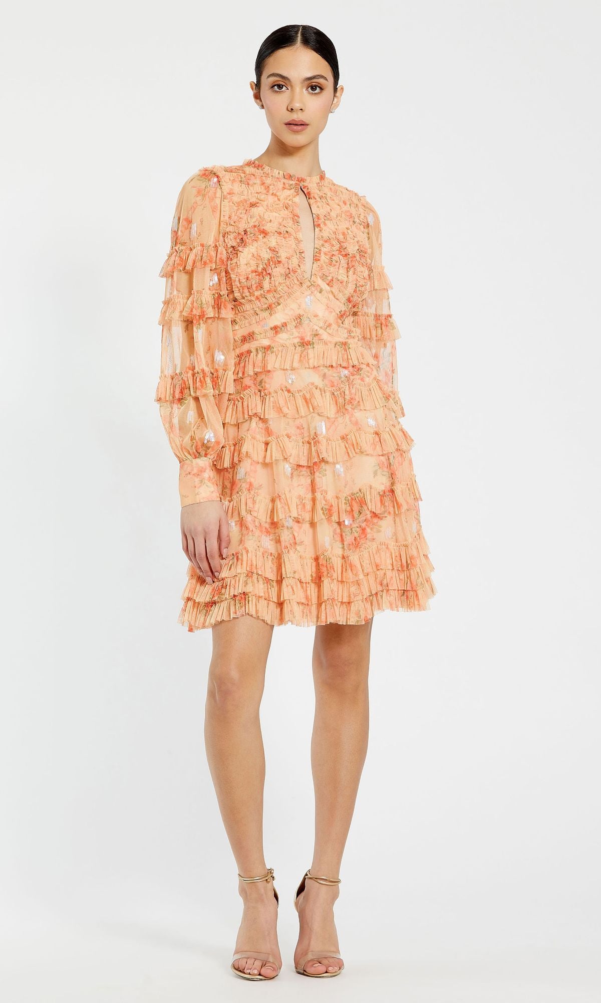 A woman models the Mac Duggal 8094 peach floral mini ruffle dress with long sleeves and a keyhole neckline—perfect for wedding guests—styled with open-toe heels against a plain white background.