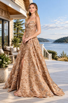A woman wears a mocha-colored Long Prom Dress: Amelia Couture 8098 featuring a strapless corset bodice, floral metallic embroidery, and a high slit on a deck overlooking a bay.