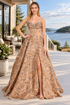 A woman wears an Amelia Couture 8098 strapless, gold, floral jacquard prom dress with a corset bodice, floor-length hem, and a high leg slit.