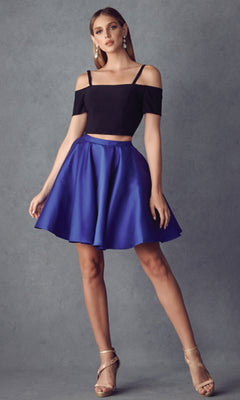 A woman stands against a gray backdrop wearing the Juliet 809 short party dress—an off-the-shoulder black crop top with thin straps and a flared royal blue A-line skirt—paired with gold strappy heels and dangling earrings.