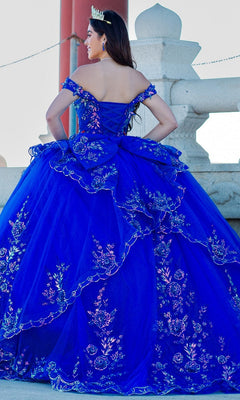 Wearing the Quinceanera Ball Gown 8100J in bright blue with iridescent beads and a tiara, a person stands outdoors with their back to the camera.