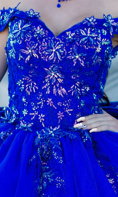 Someone wearing the Quinceanera Ball Gown 8100J, a bright blue off-the-shoulder dress featuring sequined floral patterns, iridescent beading, and a tulle skirt.