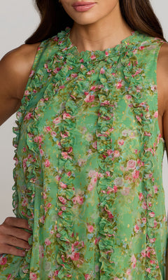 Woman modeling the Mac Duggal 8103 Midi Floral Wedding Guest Dress, a sleeveless green semi-formal chiffon dress with ruffles; posing with one hand on her hip and face partially out of frame.