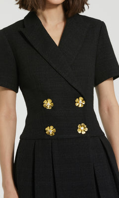 A woman wears the Mac Duggal 81038 Short Tweed Blazer Dress, featuring short sleeves, a deep V-neckline, gold floral embellishments, and a pleated A-line skirt.