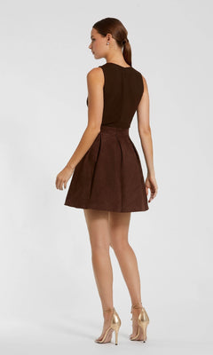 A woman faces away, wearing the Mac Duggal 81071 short brown wedding-guest dress with pleats, paired with gold high-heeled shoes.