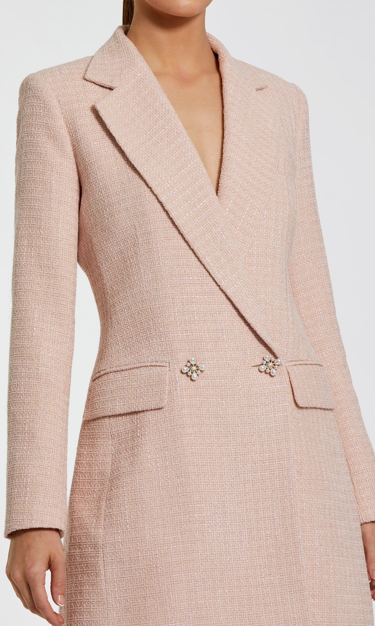 A woman wears the Mac Duggal 81198 Short Pink Wedding Guest Dress, a long-sleeve blazer style with a textured finish, deep V-neckline, two flap pockets, and jeweled buttons at the waist—an ideal pink party dress.