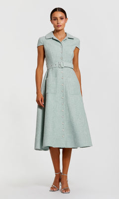 A woman stands against a white background wearing the Mac Duggal 81199 Collared Midi Green Career Dress—light green, short-sleeved, button-front with waist belt—paired with silver heels.