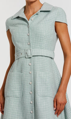 A person wearing the Collared Midi Green Career Dress: Mac Duggal 81199—featuring short sleeves, a belted waist, front buttons, and two large pockets—creates a chic and professional office look.