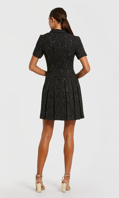A woman stands facing away in the Mac Duggal 81200 Tweed-Blazer Short Party Dress with a pleated skirt and beige heels, perfect for semi-formal events, set against a plain white background.