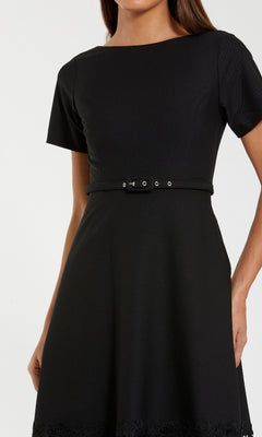 A woman wearing the Mac Duggal 81206 Short Sleeve Midi Cocktail Dress, black with cut-out details and a belted waist, shown from shoulders to mid-thigh.