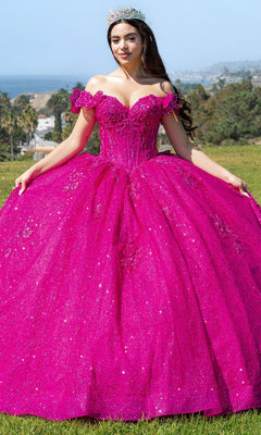 A woman in the sparkling bright pink Quinceanera Ball Gown 8120J with an off-the-shoulder design and a tiara stands outdoors on grass, framed by trees and hills.