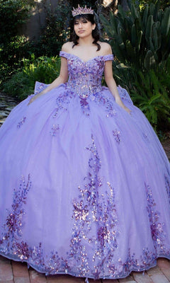 A young woman wearing the Quinceanera Ball Gown 8125J, an off-the-shoulder dress with a lace-up corset bodice and sparkling purple details, poses outdoors on a brick path with greenery, complemented by a matching tiara.