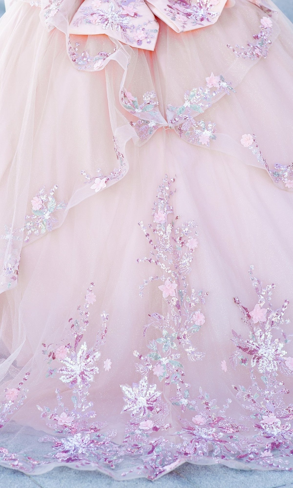 The Quinceanera Ball Gown 8125J features pink tulle, delicate floral embroidery, sequins in pastel pink, lavender, silver, and an elegant corset lace-up bodice.
