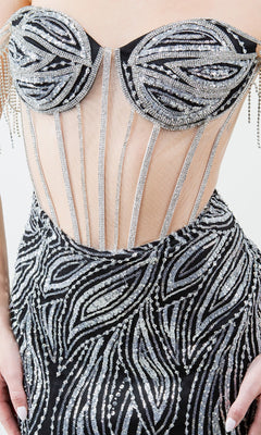 A close-up of a person wearing the Long Beaded Prom Dress: Cinderella Couture 8147J, a formal black gown with silver sequin patterns, sheer panels, and structured bodice detailing.