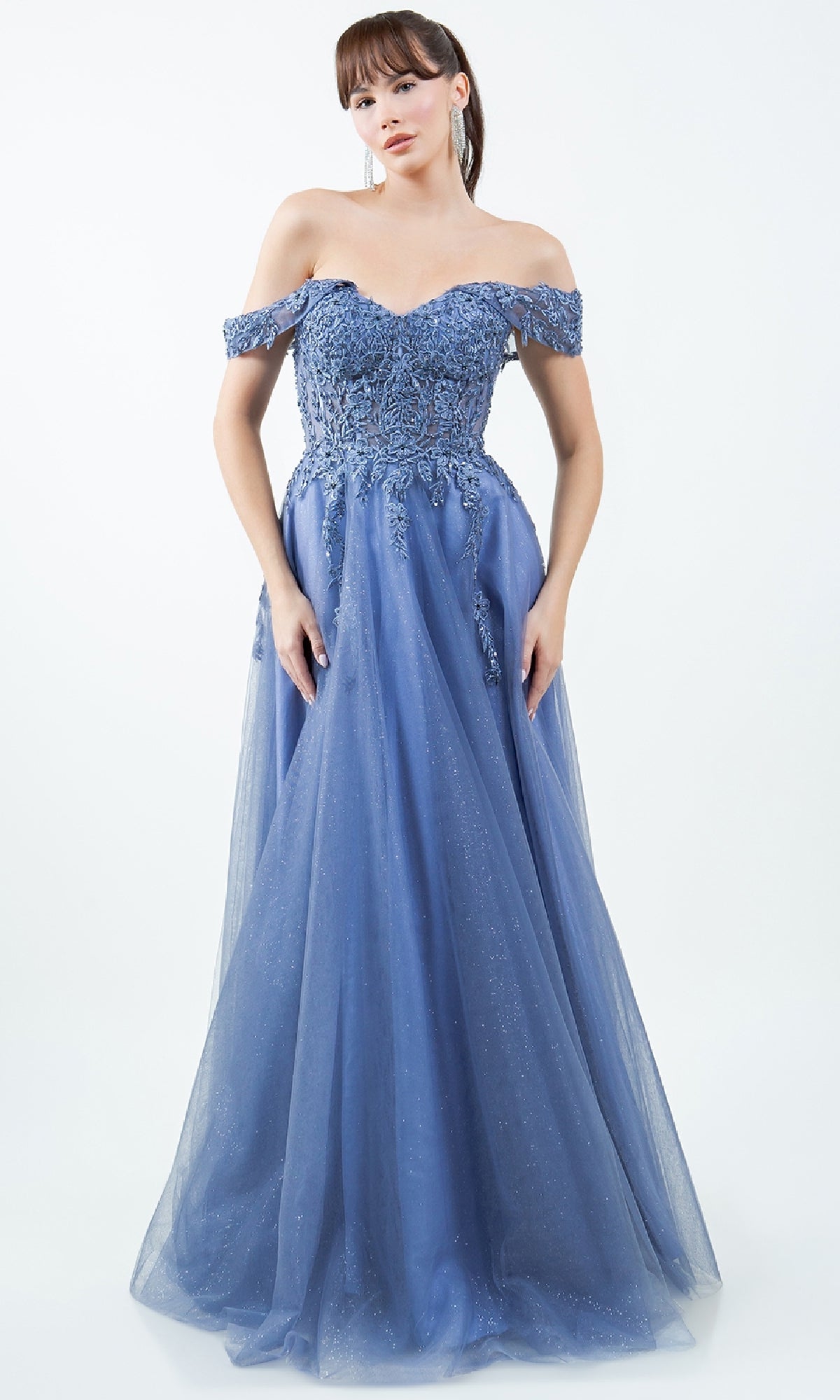A woman wears the Long Prom Ball Gown: Cinderella Couture 8152J, a blue, floor-length A-line dress with off-the-shoulder floral lace and a tulle skirt, set against a plain light background.