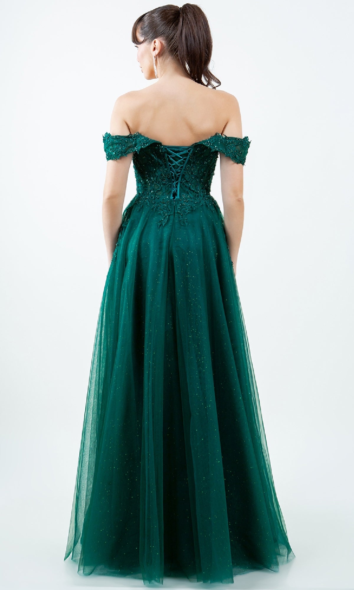 A woman stands facing away from the camera in the Cinderella Couture 8152J—a floor-length green off-the-shoulder prom ball gown with a lace-up back, subtle glitter, and embroidered-lace accents.