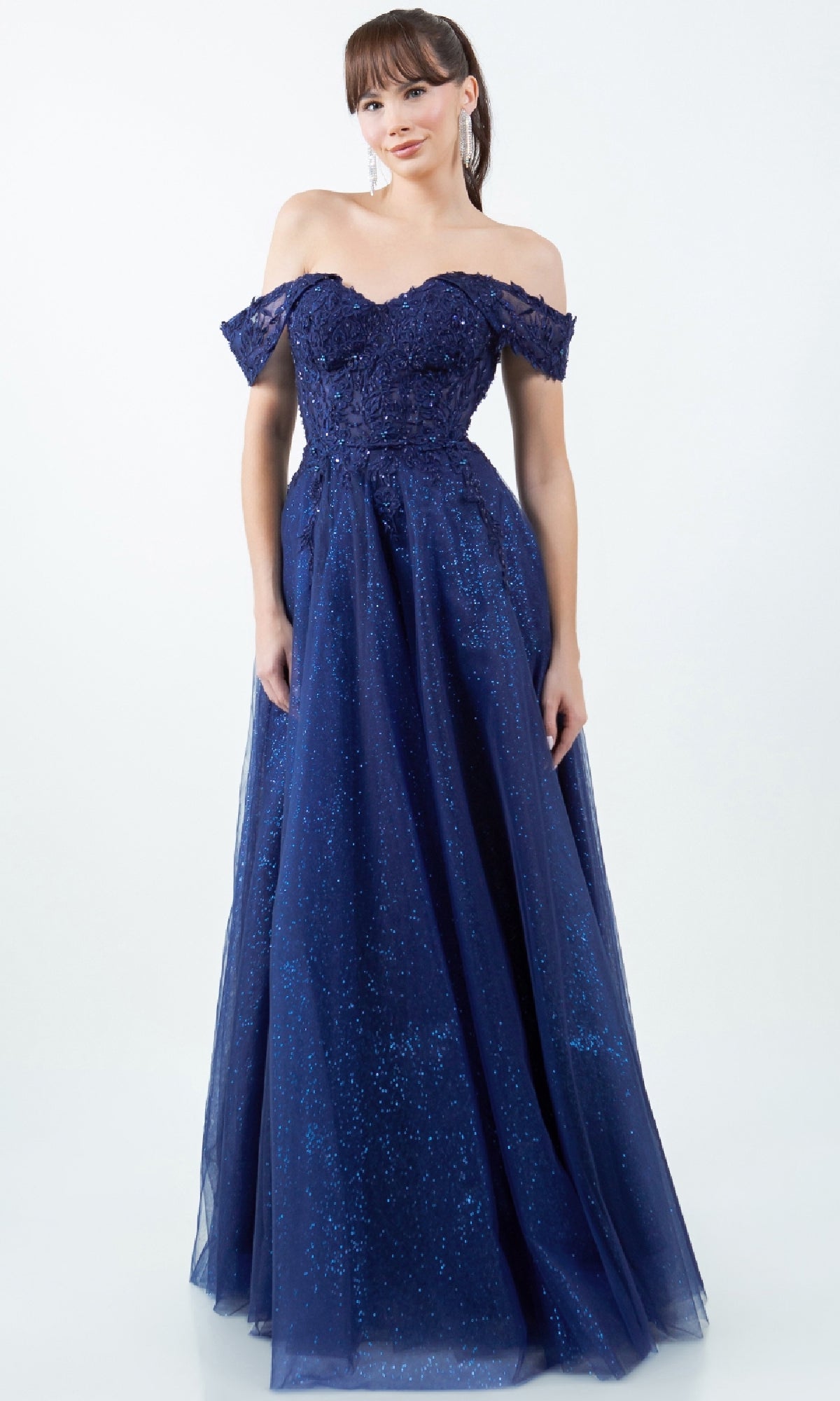 A woman stands against a plain light background wearing the Cinderella Couture 8152J Long Prom Ball Gown, an off-the-shoulder, floor-length navy blue dress with glittery details.