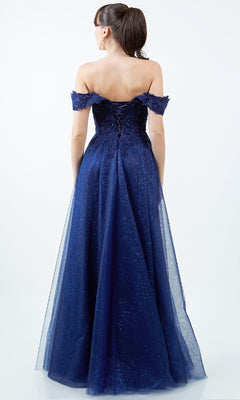 A woman wears the Cinderella Couture 8152J long prom ball gown in navy blue, featuring an off-the-shoulder neckline, lace-up corset back, and a floor-length glittery tulle skirt as she stands facing away.