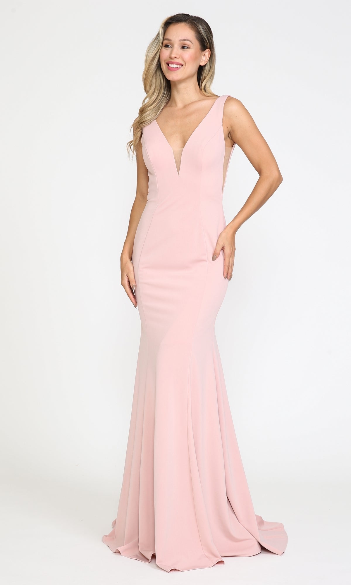 A woman stands smiling against a plain white background, wearing the Sleeveless V-Neck Long Formal Prom Dress 8158 in floor-length light pink with a deep V neckline.