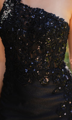 Close-up of a person wearing the One-Shoulder Prom Gown: Cinderella Couture 8162J, a black long dress with sequins and beaded floral patterns—an elegant evening gown perfect for special occasions.