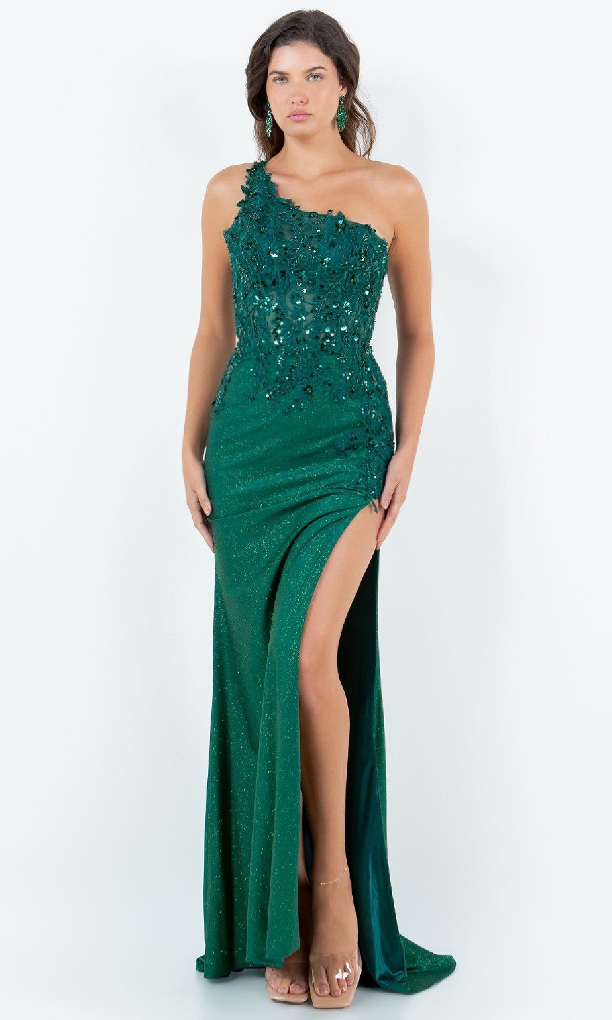 A woman poses in the Cinderella Couture 8162J—an emerald green, one-shoulder prom gown with sequins and a high slit. This stunning evening dress is perfect for formal events and is available for under $200.