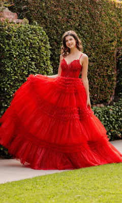 A woman stands outdoors by a tall green hedge, posing in the Cinderella Couture 8163J Glitter Prom Ball Gown—a voluminous, tiered red dress with spaghetti straps and a beaded corset bodice, radiating elegant charm.