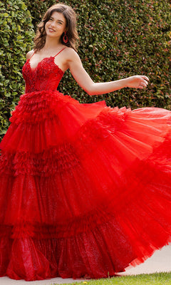 A woman stands outdoors before green hedges, her Glitter Prom Ball Gown: Cinderella Couture 8163J—a bright red, ruffled, floor-length dress with a beaded corset bodice—elegantly fanned out to the side.