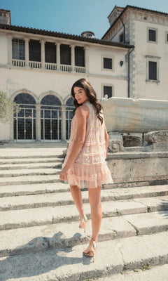 Wearing the Mac Duggal 8172 Short Party Dress, a woman in heels walks up stone steps outside a large, elegant building with arched windows.