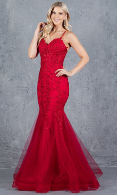 A woman poses confidently before a gray textured backdrop in the Lace-Up Long Prom Dress: Cinderella Couture 8175J, a red evening gown with beaded lace applique and thin straps, one hand on her hip and the other touching her hair.