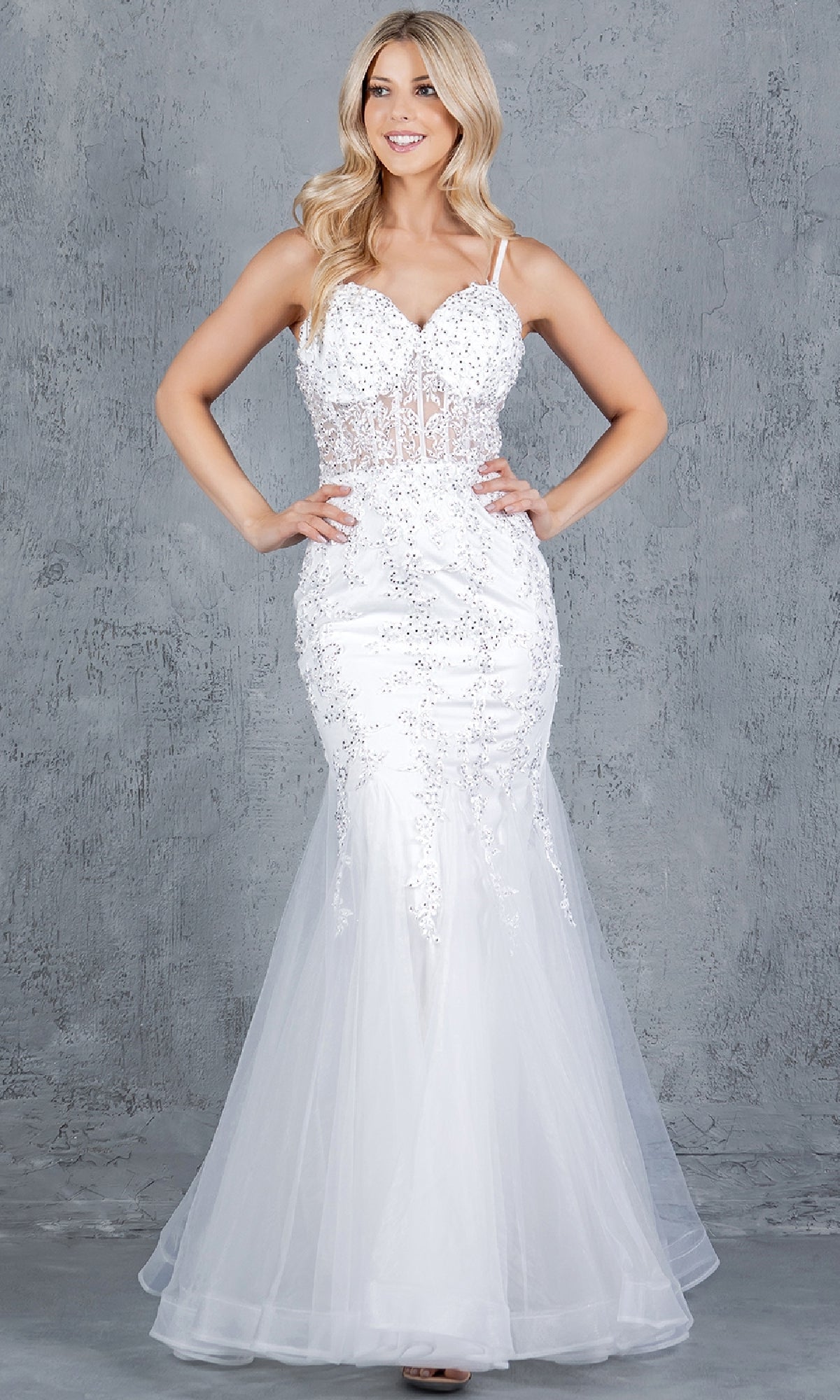 A woman stands before a gray textured wall wearing the Cinderella Couture 8175J, a sleeveless lace-up mermaid prom dress with beaded embellishments and a flowing tulle skirt.