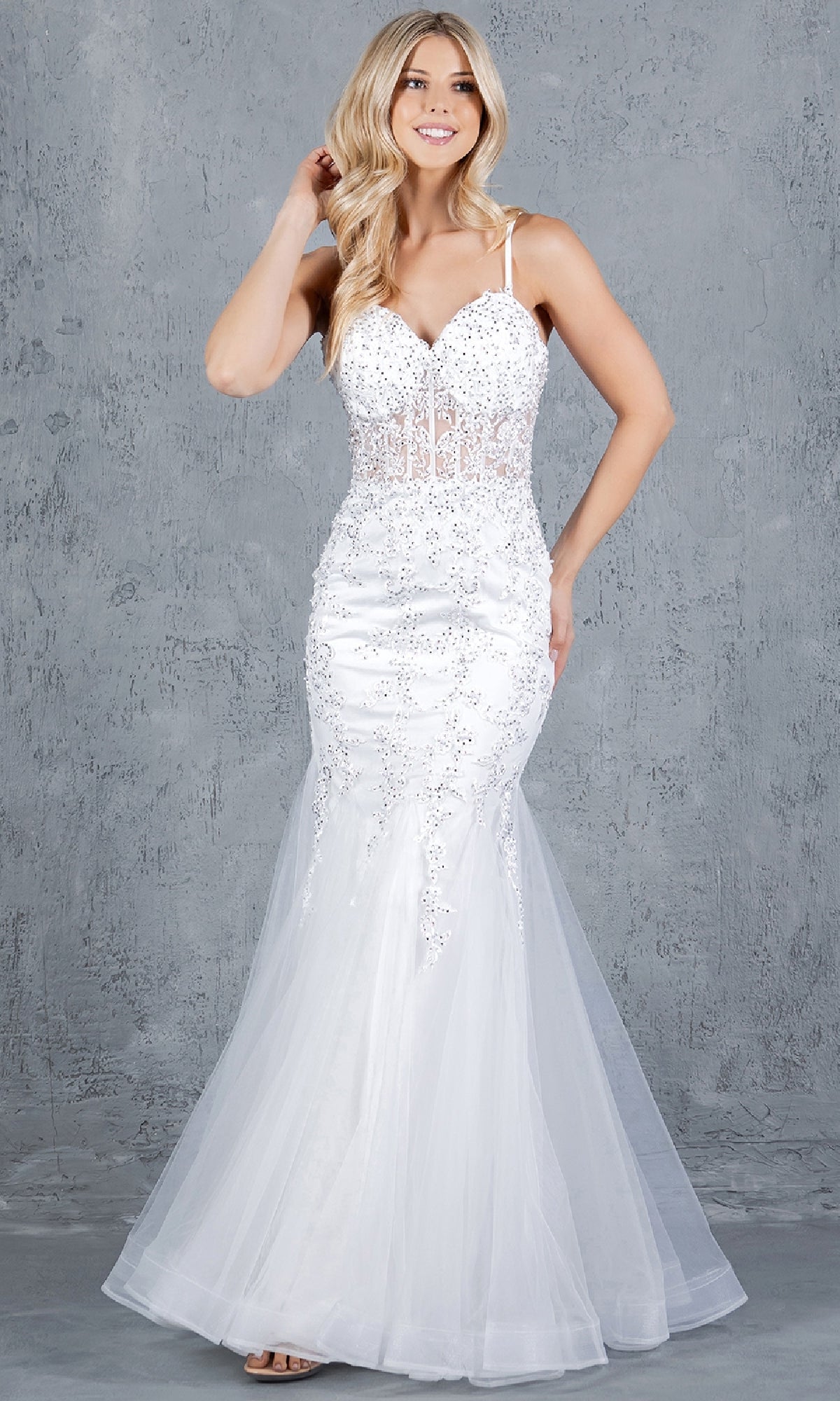 A woman stands before a gray textured background wearing the Lace-Up Long Prom Dress: Cinderella Couture 8175J, a sleeveless mermaid gown with beaded lace applique, sequin embellishments, and a flowing tulle skirt.