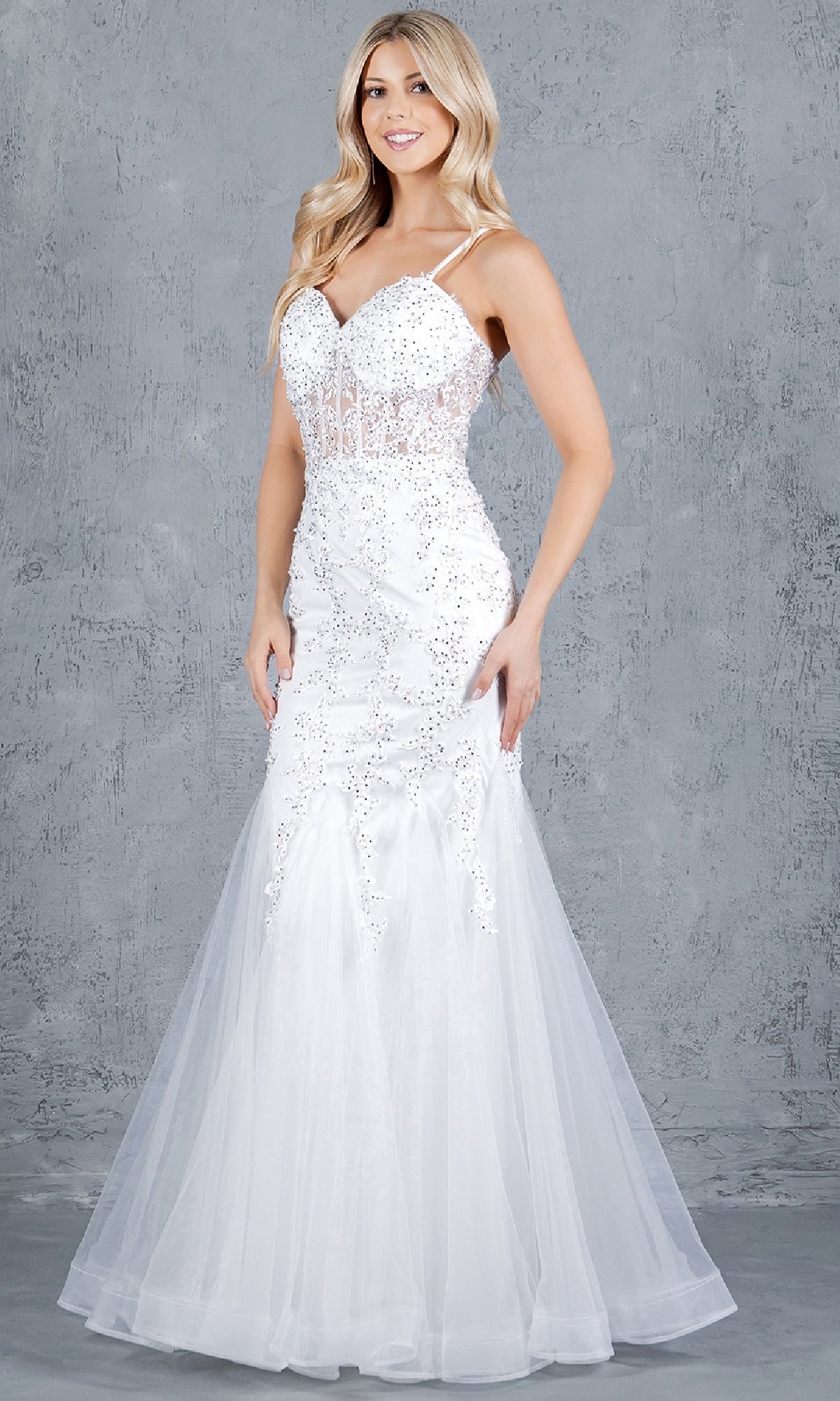 A woman stands against a gray textured background wearing the Cinderella Couture 8175J, a strapless fitted white lace-up long prom dress with sequin embellishments and a mermaid silhouette.