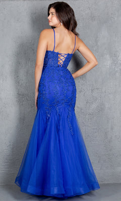 A woman stands against a gray textured wall, wearing the Lace-Up Long Prom Dress: Cinderella Couture 8175J in royal blue with beaded lace applique and floral embellishments.